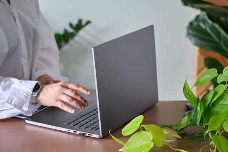 Womens hands at a laptop against a background of greenery.