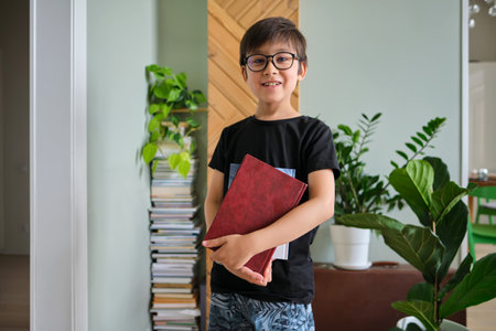 A boy holds a stack of books against the background home library.の写真素材