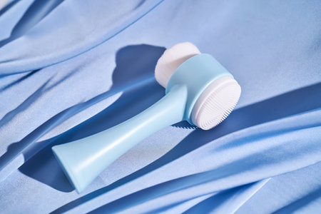 Blue brush-massager for the face on a background of blue silk.