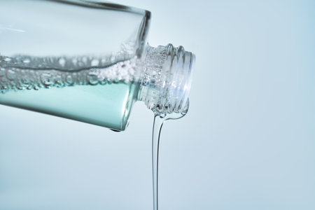 Cosmetic bottle from which serum is pouring on a blue background.