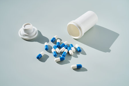 Blue and white capsules spilled out of a medicine jar on a blue background.の写真素材