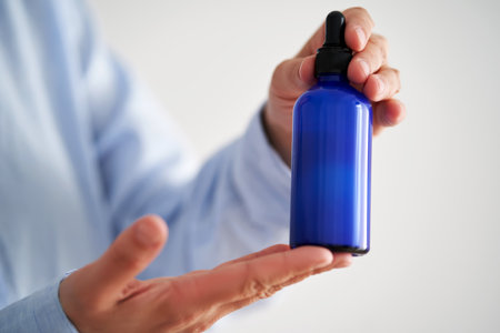 Female hands in a blue shirt hold a blue bottle of serum.の写真素材