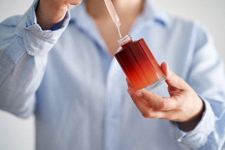 Female hands in a blue shirt hold a pink bottle of serum.の写真素材