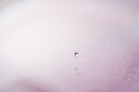 Serum or cosmetic oil flows into a transparent bowl on a purple background.