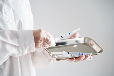 Anonymized photo of a doctors hands holding a tray and a syringe with a needle.の写真素材