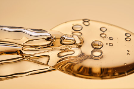 A beautiful drop of gel-like cosmetic serum with bubbles on a golden background.