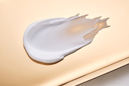 Swatch with white cream texture on a golden background.