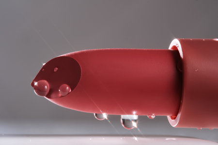 Classic lipstick with drops of water on a neutral background.の写真素材