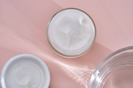 An open jar of cream with its texture on a pink background.