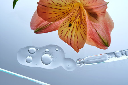 A pipette with a beautiful drop of serum on a background of lily flowers.の写真素材