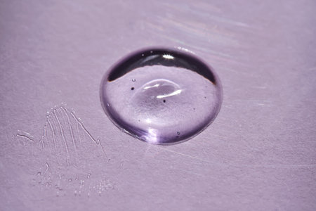 A drop of oil serum on a purple background with beautiful highlights.の写真素材