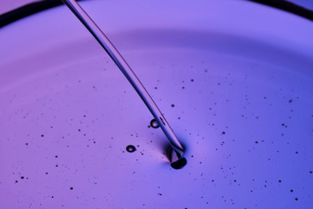 A jet of facial oil flowing into a petri dish on a purple background.