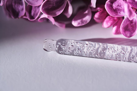 Cosmetic pipette with serum and lilac flowers on a purple background.の写真素材