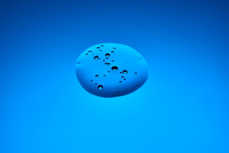 A drop of cosmetic product or serum on a blue background.