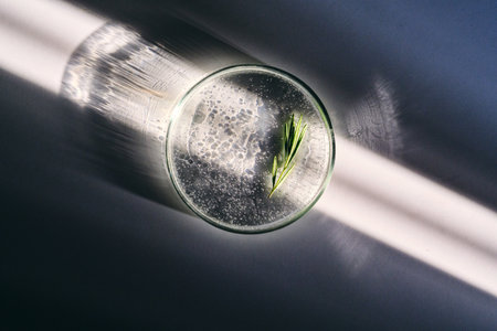 Petri dish with rosemary serum on a white background in the sun with a beautiful shadow..