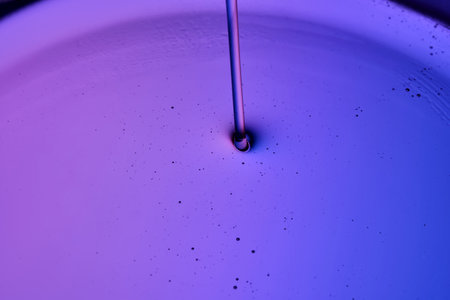 Serum or body cream flows into a petri dish on a purple background.