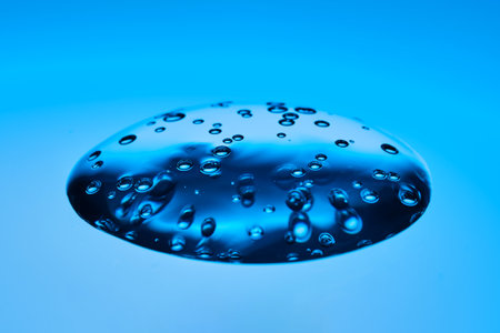 The viscous gel serum for the face flows and collects into a drop on a blue background..の写真素材