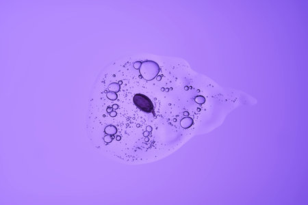 A drop of cosmetic serum with bubbles and a purple petal.の写真素材
