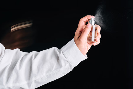 A hand in a white shirt sprays perfume or air freshener. Black background.の写真素材