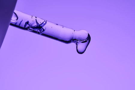 A juicy drop of serum hangs on the pipette, demonstrating the texture of the cosmetic product.