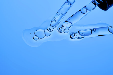 Two pipettes with facial serum pouring out of them on a blue background.