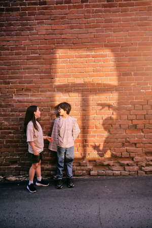 Children having conversation by brick wall in sunlight.の写真素材