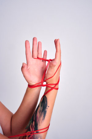 Hands tied with red string symbolizing limitationの写真素材