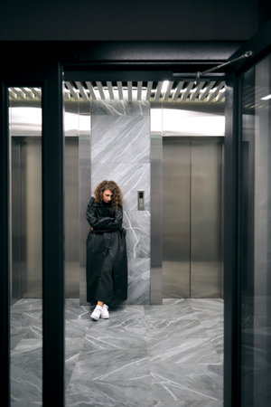 Woman waiting sadly in modern elevator lobbyの写真素材