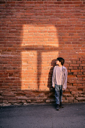 Boy standing enjoying warm light on brick wallの写真素材