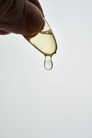 Hand squeezing omega 3 capsule releasing oil dropの写真素材