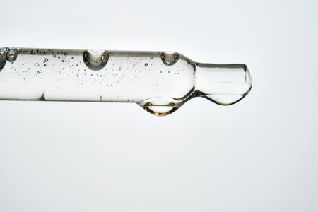 Pipette containing transparent liquid serum with small bubbles, forming a drop. Ideal for beauty, skincare, and medical conceptsの写真素材