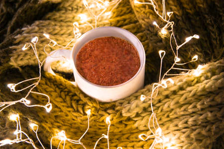 Close-up of hot chocolate between a woolen blanket and Christmas lights. Winter concept at home. Horizontal photographyの写真素材