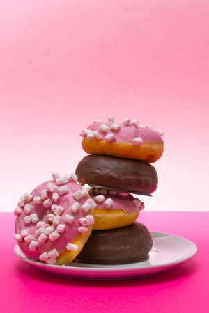 Close-up of a white plate of pink donuts with cumin and chocolate covered. Vertical photographyの写真素材