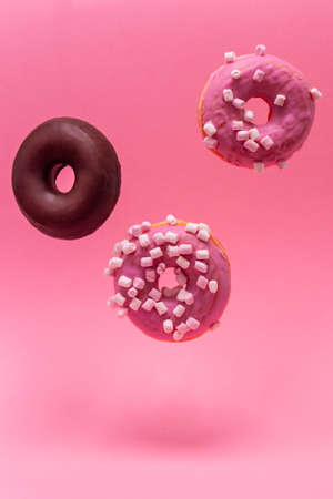 Close-up of three donuts, two roses and one chocolate, levitating on a pink background. Vertical photographyの写真素材