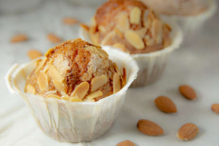 Close-up of three muffins on a wooden table with a white tablecloth and several almonds. Horizontal photographyの写真素材