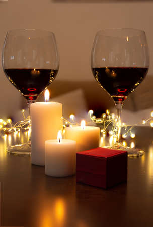 Romantic dinner scene at home: candles, box with a jewel and two glasses of wine. Concept of Valentine's Day at home and new normal. Horizontal photographyの写真素材
