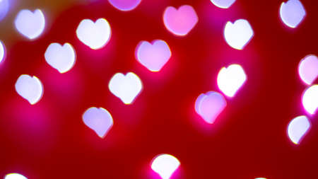 Background of different colors defocused lights with a heart shape on a red background. Abstract...
