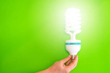 Close-up of a hand holding a lit led bulb against a green background. Concept of energy saving at home. Copy spaceの写真素材