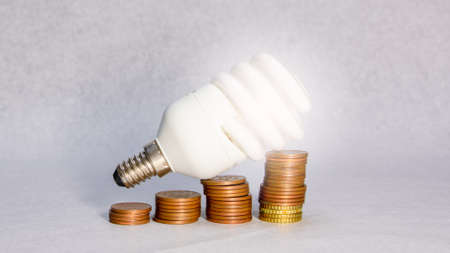 Close-up of a led light bulb on various coins on white background. Concept of energy saving at home.