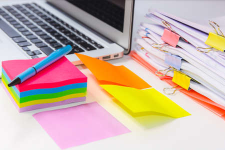 Close-up of a pile of papers with a post-notebook, colored post its and a pen. Information overload...