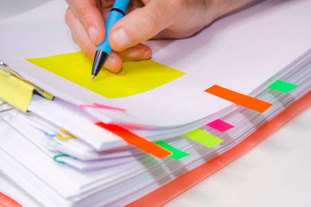 Close-up of a hand writing on a yellow paper. Horizontal photography. Information overload conceptの写真素材
