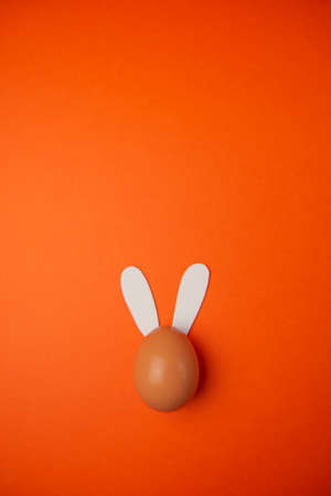 Aerial shot of an egg with rabbit ears on an orange background. Easter egg with bunny ears.の写真素材