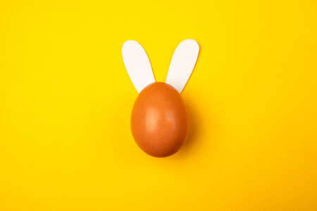 Aerial shot of an egg with rabbit ears on an yellow background. Easter egg with bunny ears.の写真素材