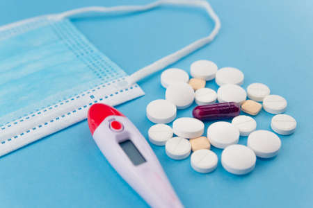 Overhead shot of several pills, a thermometer, and a surgical mask. Concept of drugs for the...