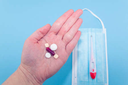 Overhead shot of a hand holding several pills, in the background a thermometer and a surgical mask. Concept of drugs for the treatment of diseases, especially against Covid-19の写真素材