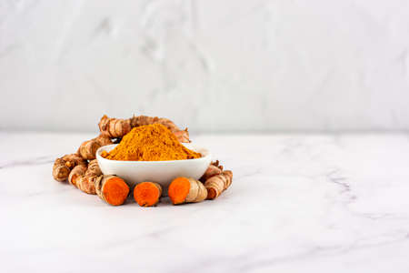 Bowl with turmeric powder with several roots of the same plant on a marble table. Concept of natural medicine and homeopathyの写真素材