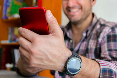 Wide shot of a man in front of a smartphone, making a video conference and smiling. Concept of teleworking from home. Concept of telecommuting from home.の写真素材