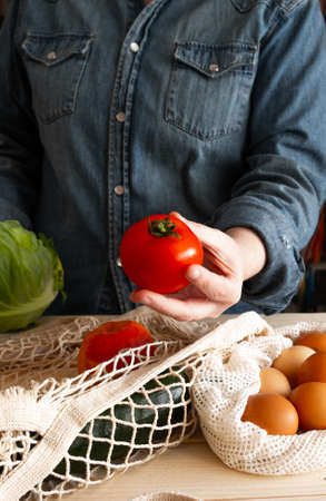 Woman picking up sustainably made shopping with cardboard and cloth bags, holding a tomato. Plastic free. Waste zeroの写真素材