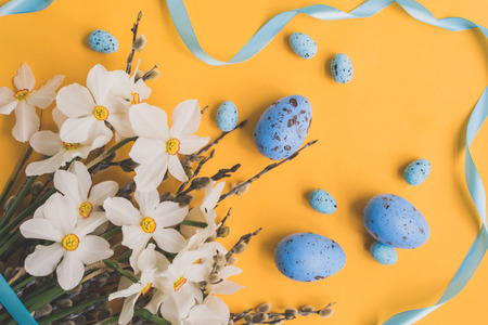 Easter eggs willow branches and white daffodils on a yellow backgroundの写真素材