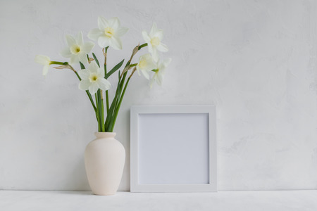 Mockup with a white frame and white daffodils in a vase on a light backgroundの写真素材